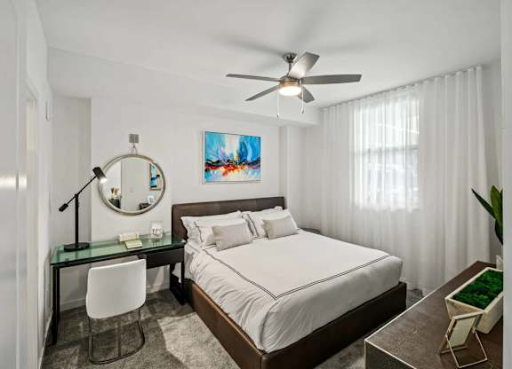A bedroom with a bed, desk, chair, and a ceiling fan.