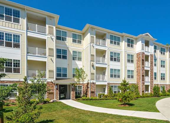 A large white apartment building with balconies and a green lawn in front.