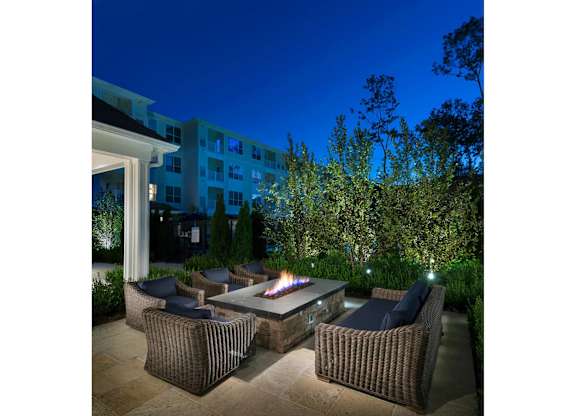 A patio with a fire pit surrounded by chairs and plants.