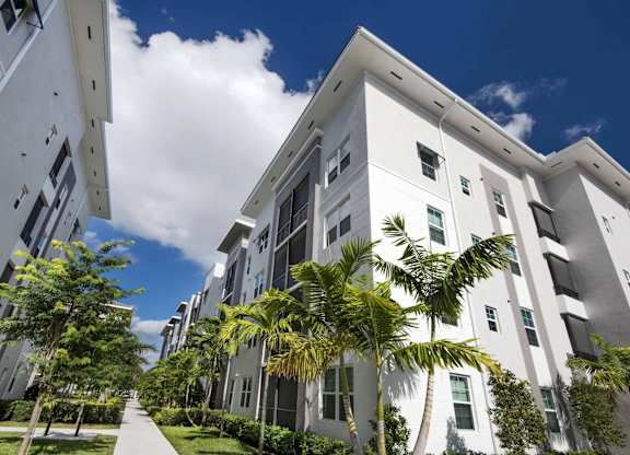 A modern white building with a balcony is surrounded by trees.