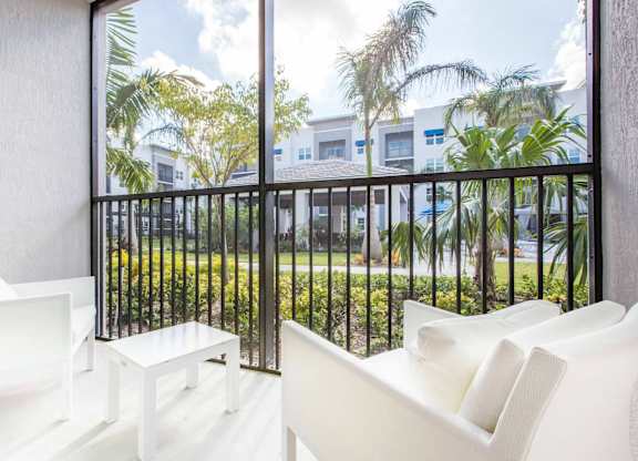 A white chair is in front of a balcony with a view of a green lawn and trees.