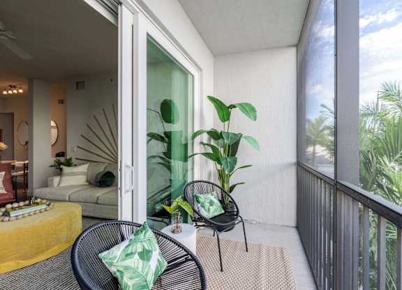 A balcony with a table and chairs overlooking a lush green area.