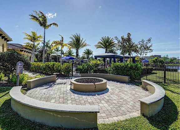 A circular brick patio with a fire pit in the middle, surrounded by a low wall and palm trees.