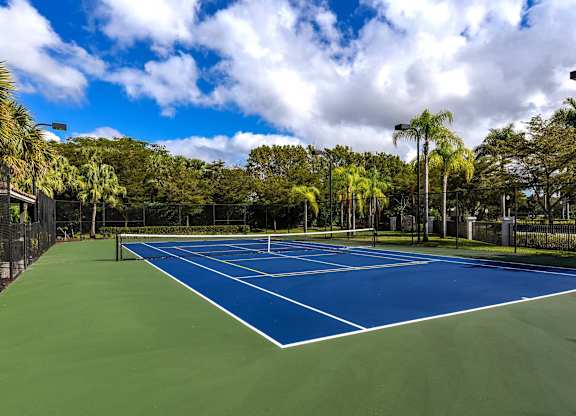 A tennis court surrounded by trees and a fence.