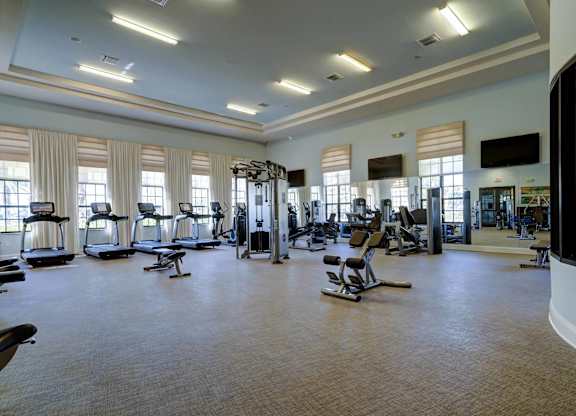 A spacious gym with various exercise equipment and a flat screen TV mounted on the wall.