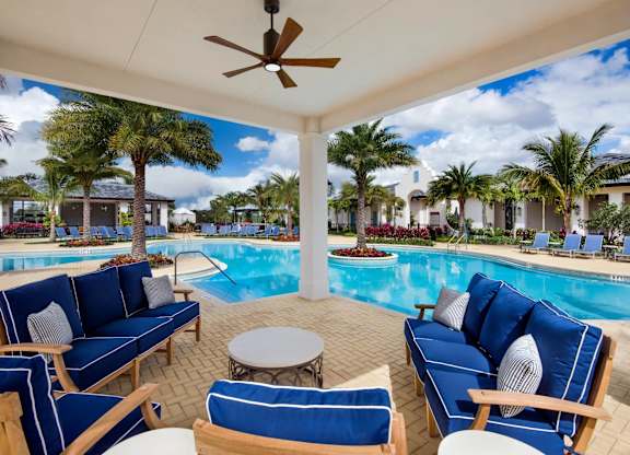 A poolside patio with blue couches and a ceiling fan.