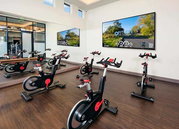 A room with a row of stationary bikes and a TV showing a fitness app.