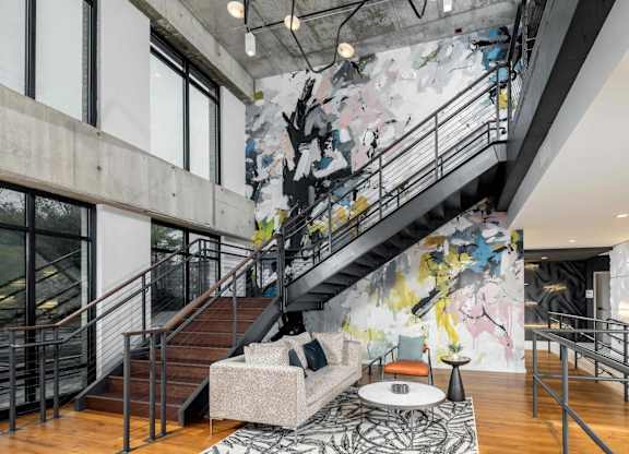 A large mural of a tree with a bird on it is on the wall above a staircase.