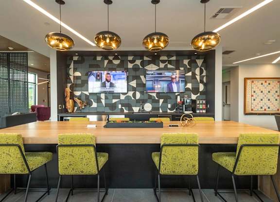 A conference room with a long table and chairs, a television screen, and hanging lights.