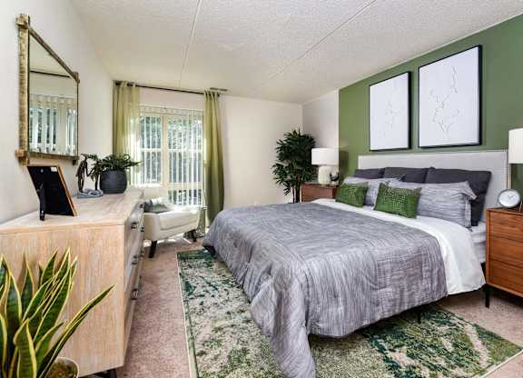 A bedroom with a bed, nightstand, and a plant.