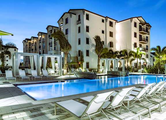 A large swimming pool with lounge chairs in front of a multi-story building.