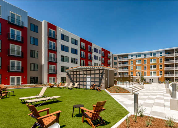 A modern outdoor seating area with wooden chairs and tables is surrounded by multi-story buildings.