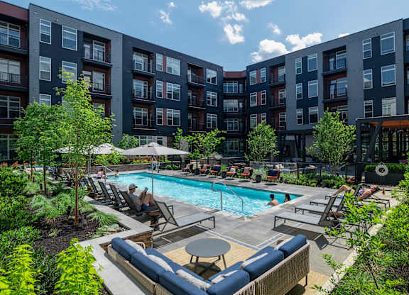 A swimming pool surrounded by lounge chairs and umbrellas in a courtyard.