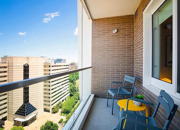 A balcony with a table and chairs overlooks a courtyard and buildings.