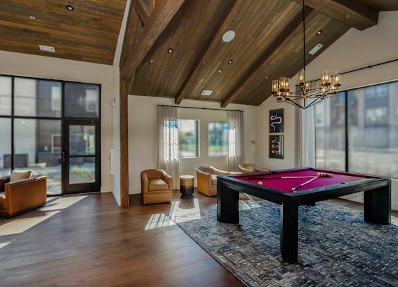 A pool table is in the middle of a room with a high ceiling and a lot of windows.