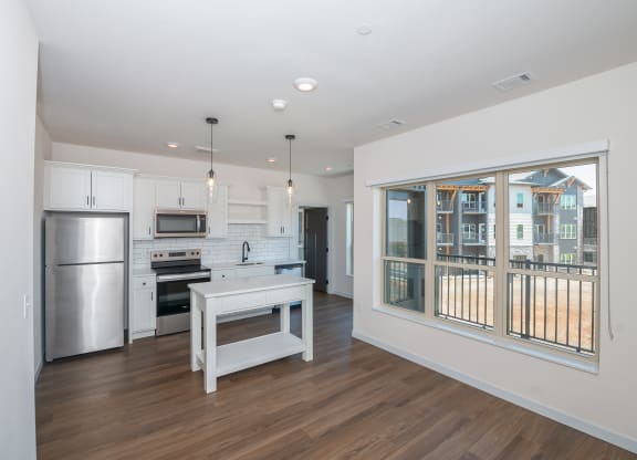 a living room with a large window and a kitchen with stainless steel appliances at The Crossings  at Windsong, Prescott Valley, 86314