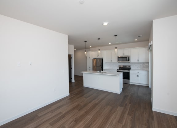 an empty living room and kitchen with white walls and wood flooring at The Crossings  at Windsong, Prescott Valley, AZ