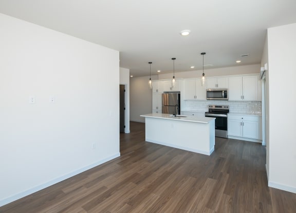 an empty living room with a kitchen with white walls and wood floors at The Crossings  at Windsong, Prescott Valley, AZ