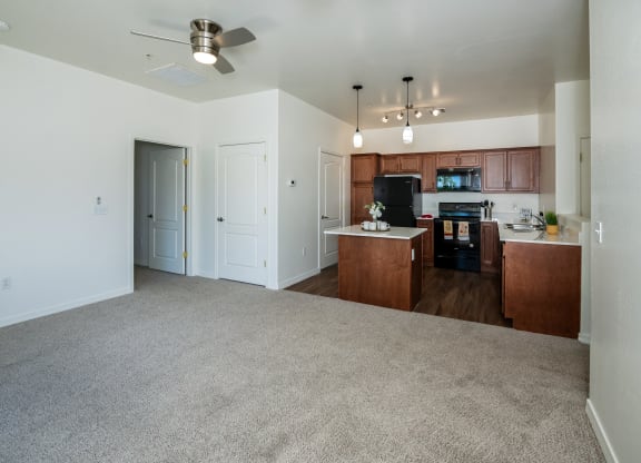 an empty living room with a kitchen and a ceiling fan