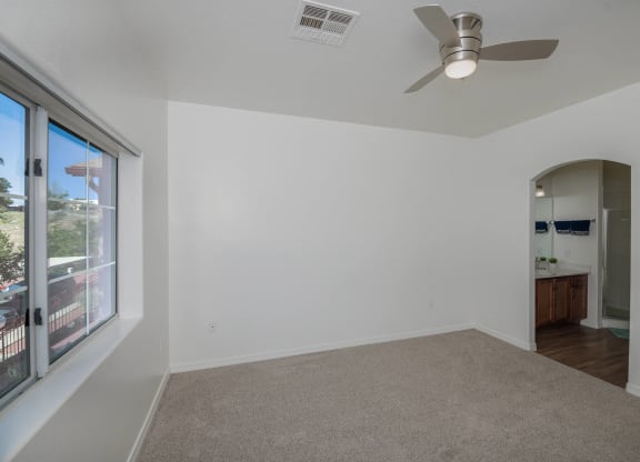 an empty living room with a large window and a ceiling fan