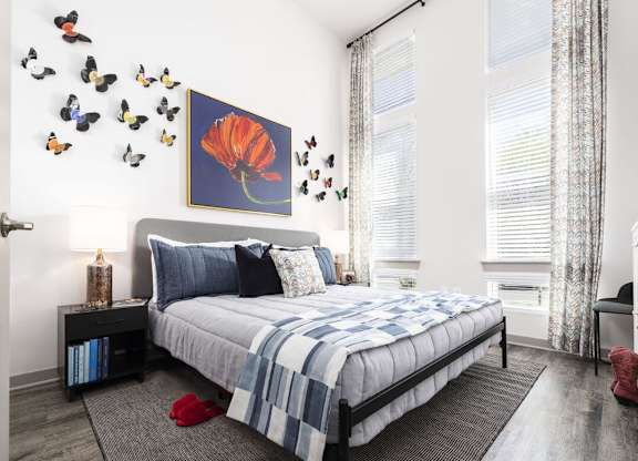 A bedroom with a bed, a painting of a flower, and butterflies on the wall.