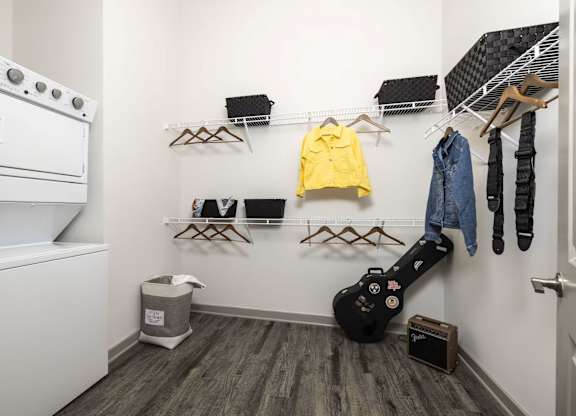 A room with a guitar and clothes hanging on the wall.