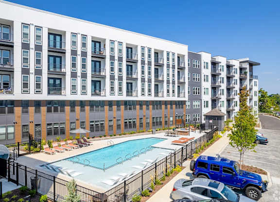 A large apartment complex with a pool and cars parked in the driveway.