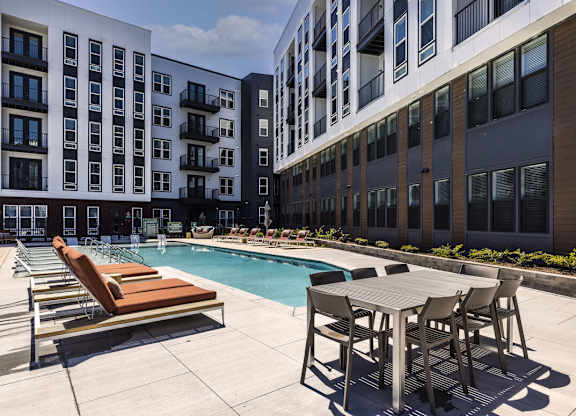 A pool area with chairs and a table in front of apartment buildings.