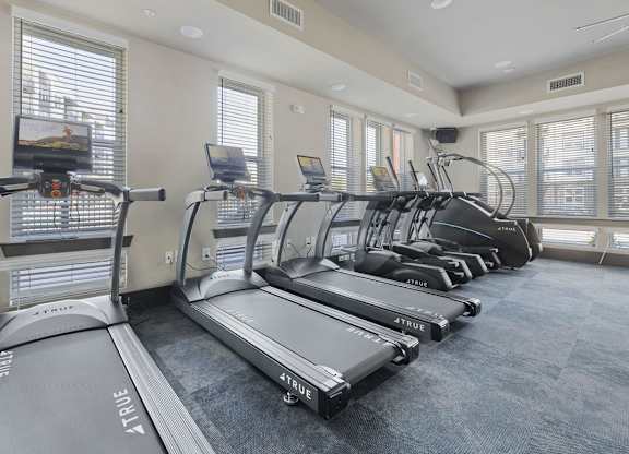 A row of treadmills in a gym with a television on the wall.