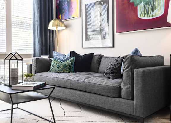 A grey couch with blue pillows and a black coffee table in front of it.