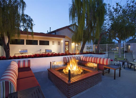 Goleta, CA, Apartments - Pacific Oaks - Gated Outdoor Lounge with Couches, Fire Pit, Grilling Stations, and Surrounding Trees.