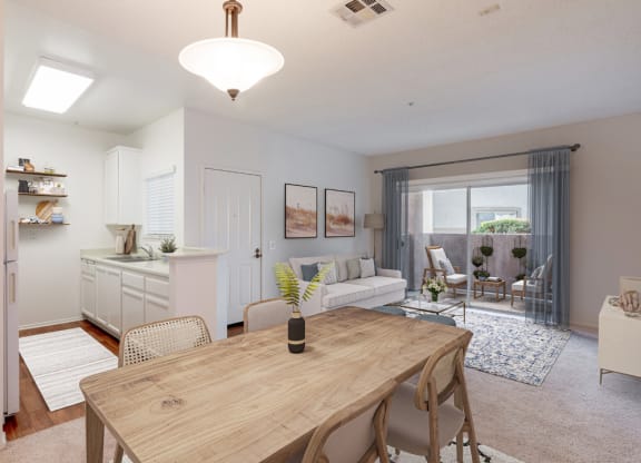 1-Bedroom Apartments in Ventura, CA - Cypress Meadows - Living Room Features A Wood Dining Table, Light Sofa Seating, Sliding Glass Doors, And A White Kitchen.