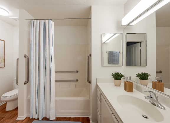 Two-Bedroom Apartments in Ventura, CA - Cypress Meadows - Bathroom With Vanity Sink, Large Mirror, Tub Shower With Grab Bars, And Blue Stripe Curtain.
