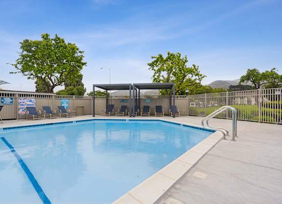 A large outdoor swimming pool with a blue tiled edge and a metal fence surrounding it.