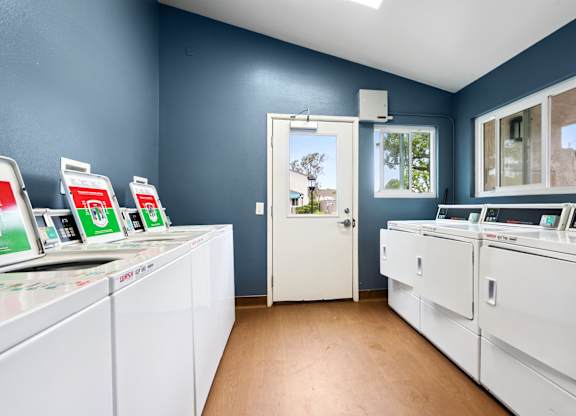 A laundromat with washers and dryers and a view of the outside.