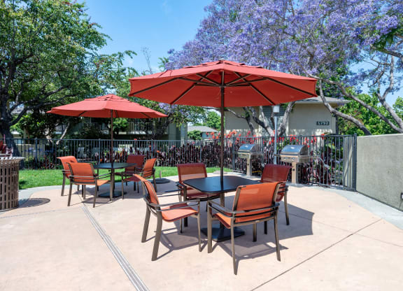 Two-Bedroom Apartments in Goleta, CA - Encina Meadows - BBQ Area with Grilling Stations, Umbrella Tables and Chairs, and Surrounding Manicured Lawn and Trees.