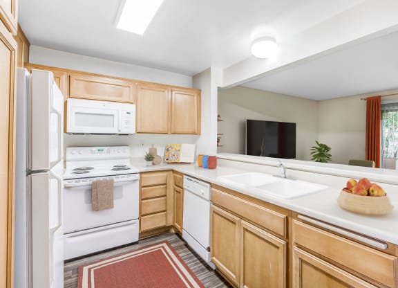 Goleta, CA, Apartments Near Trader Joe's - Encina Meadows - Kitchen With Light Wood Cabinets, White Stove And Microwave, Double Sink And Dishwasher.