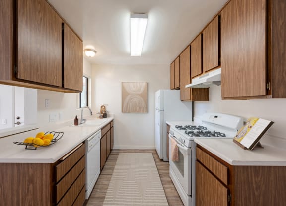 Santa Maria, CA Apartments - Knollwood Meadows - Aisle-Style Kitchen with Wood-Patterned Cabinetry, White Appliances, and White Countertops