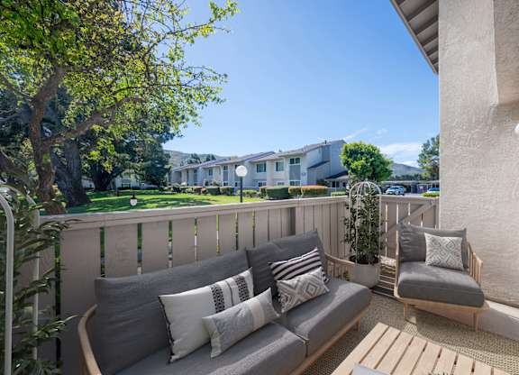 A balcony with a grey couch and pillows overlooking a building.