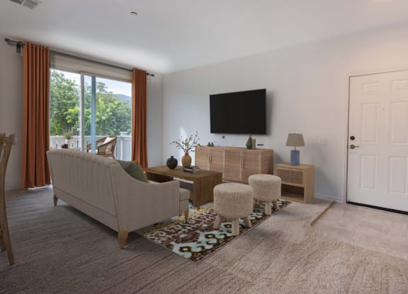 Apartments for Rent in Lompoc, CA - Oceanwood - Living Room with Carpeting, Sofa, Ottoman Stools, Coffee Table, Side Table with Lamp, TV, and Sliding Glass Door with Access to Balcony.