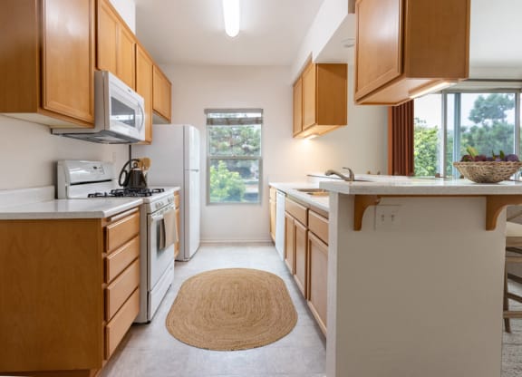 One-Bedroom Apartments in Lompoc, CA - Oceanwood - Kitchen with Refrigerator, Gas Range, Microwave Oven, Wood Cabinets, Breakfast Bar, and Bar-Style Chairs.