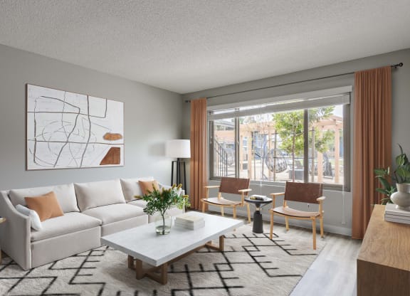 Goleta, CA, Apartments Near Costco - Patterson Place - Living Room with Wood Style Flooring, Area Rug, Couch, Armchairs, Side Table with Lamp, Coffee Table, Standing Lamp, Wall Art, and Large Window with Curtains