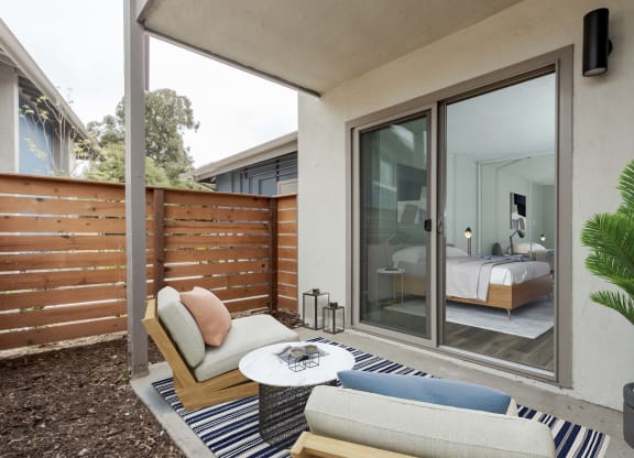 2-Bedroom Apartments in Goleta, CA - Patterson Place - Patio with Cement Floor, Area Rug, Lounge Chairs, Coffee Table, Potted Plant, Privacy Fence, and Sliding Glass Door with Access to Bedroom
