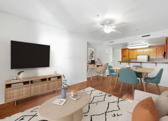 Apartments In Ventura, CA For Rent - Ralston Courtyards - Living Room With Plank Flooring, Area Rug, Couch, Coffee Table, Media Cabinet, Wall-Mounted TV, Ceiling Fan, And View Of Dining Area And Kitchen.