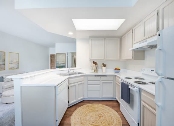 Assisted Living in Santa Barbara, CA - Rancho Franciscan - Kitchen With White Cabinetry, White Appliances, White Countertops, Flush Mount Light Fixture, and Round Natural Woven Rug