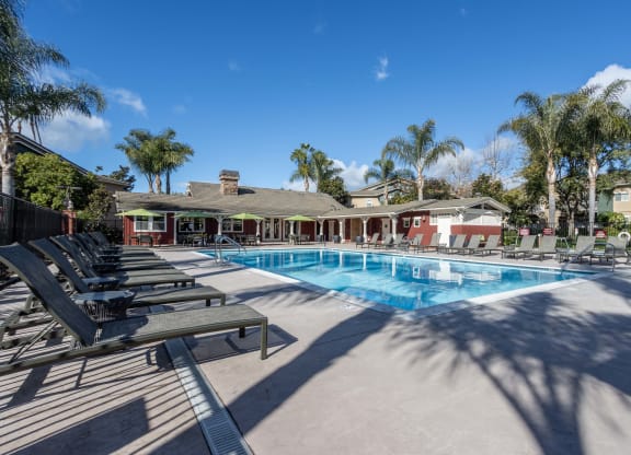 3 BR Apartments in Goleta CA - Sumida Gardens - Gated Sparkling Pool with Lounge Chairs, Green Umbrellas, and View of Clubhouse and Nearby Palm Trees