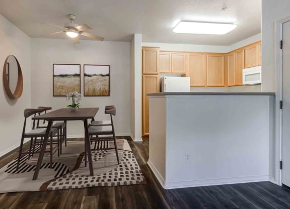 Pet-Friendly Apartments in Goleta, CA - Sumida Gardens - Dining Area with Wood-Style Flooring, Area Rug, Table and Chairs, Ceiling Fan, and View of Kitchen.