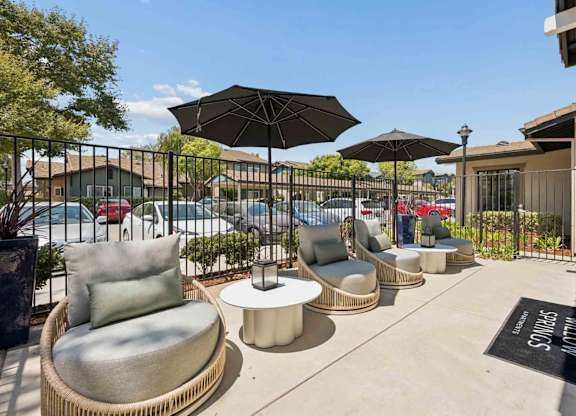 A patio with chairs and umbrellas is surrounded by a black metal fence.
