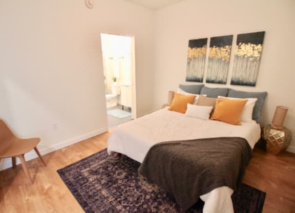 A bedroom with a bed, chair, and artwork on the wall.