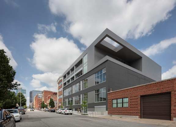 A modern building with a unique design is situated on a street with cars parked on the side.